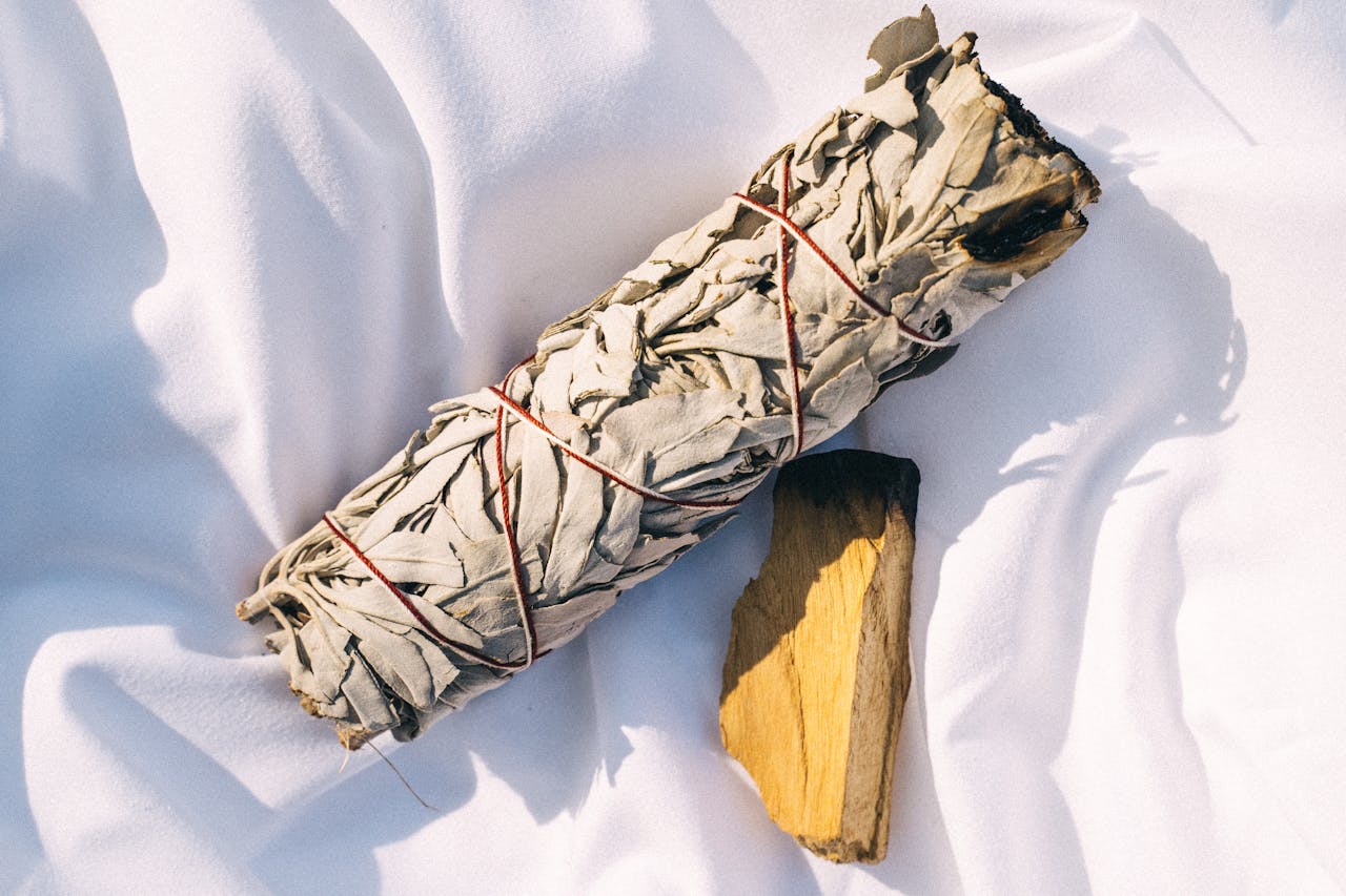 A bundle of white sage paired with palo santo wood resting on a soft white fabric for calming ambiance.